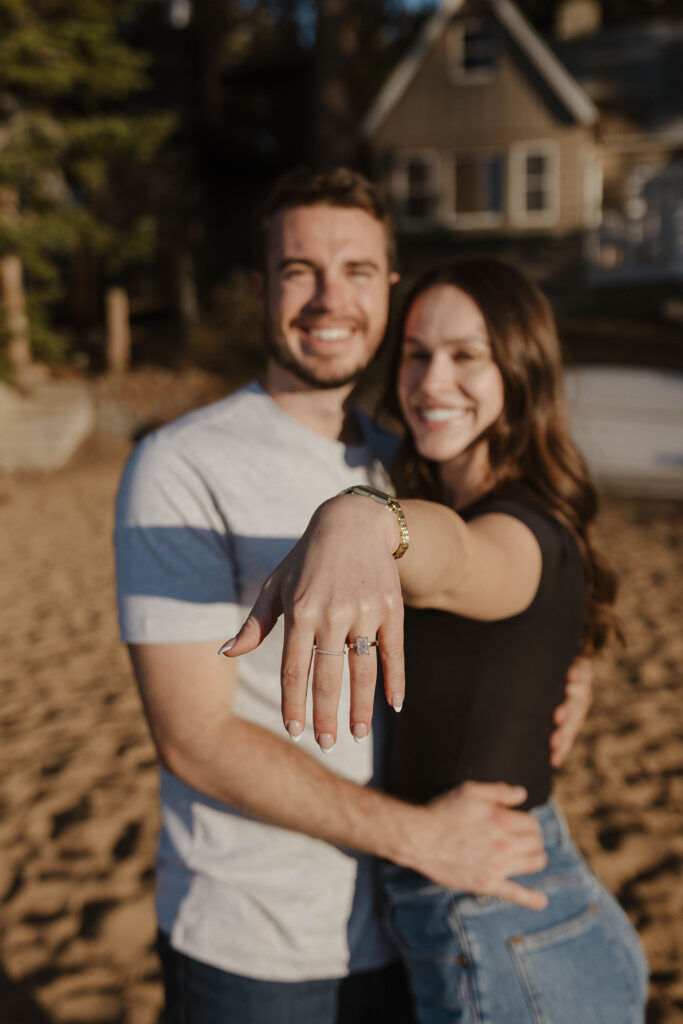 Woman showing off engagement ring on finger while hugging fiancé on a beach in Lake Tahoe
