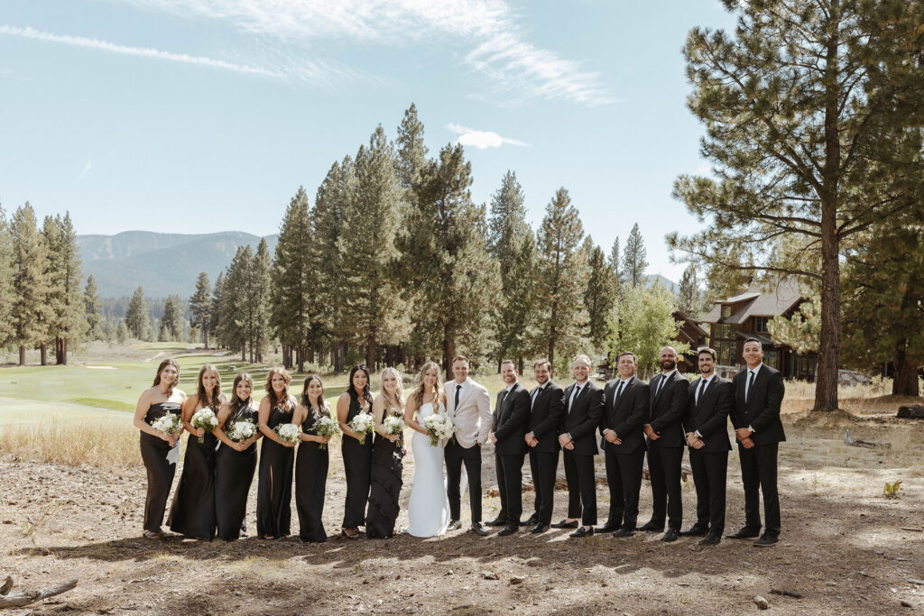 Entire wedding bridal party smiling at camera while standing in front of pine trees at Timbers at Old Greenwood