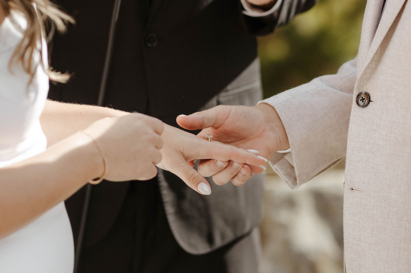 Close up of groom holding bride's hand with wedding ring during ceremony at Old Greenwood