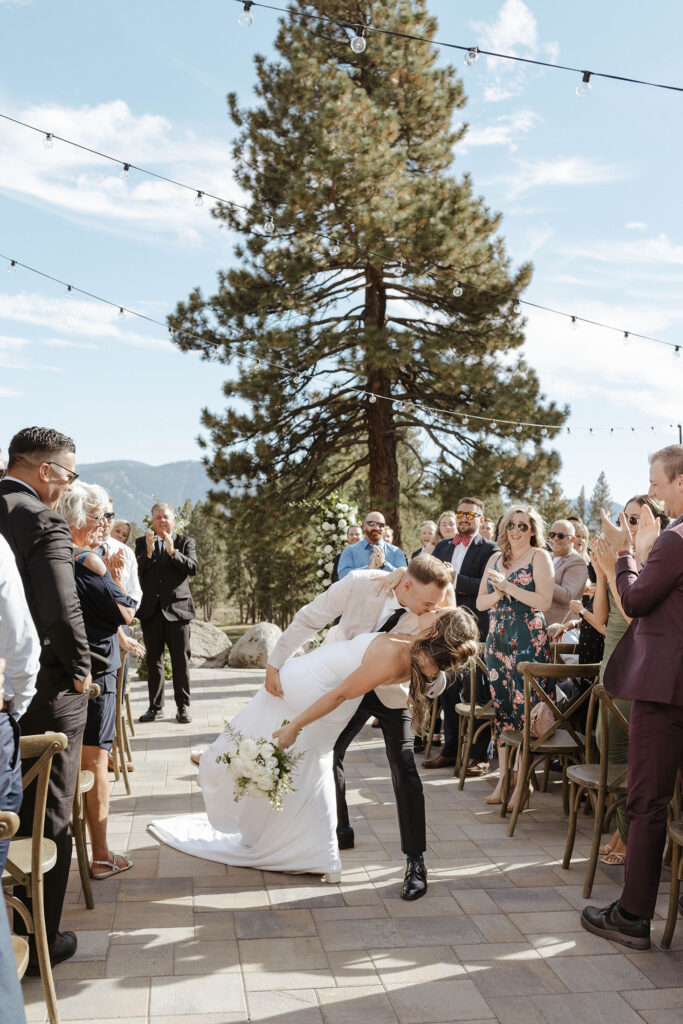 Groom holding and leaning back bride and kissing while walking down aisle after wedding ceremony at Timbers at Old Greenwood