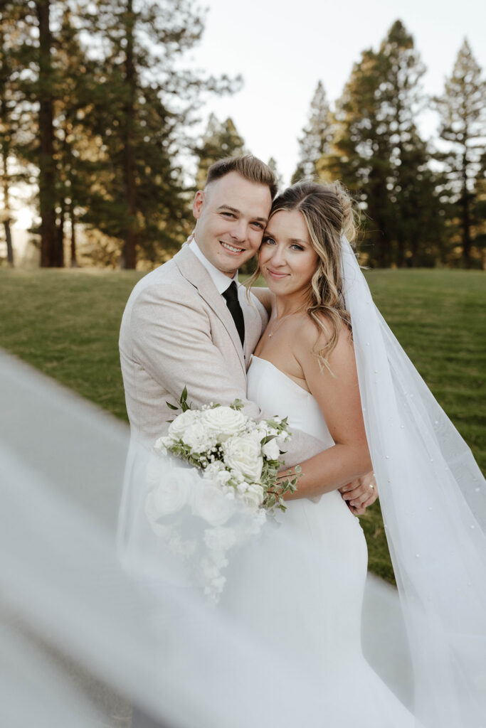 Wedding couple hugging each other while smiling at camera with veil obscuring camera lens at Old Greenwood