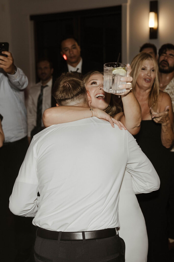 Bride smiling and dancing while holding drink and hugging groom during reception at Timbers at Old Greenwood