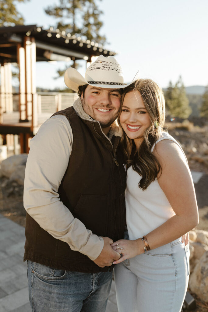 Engagement couple hugging each other and holding hands while smiling at the camera in Truckee