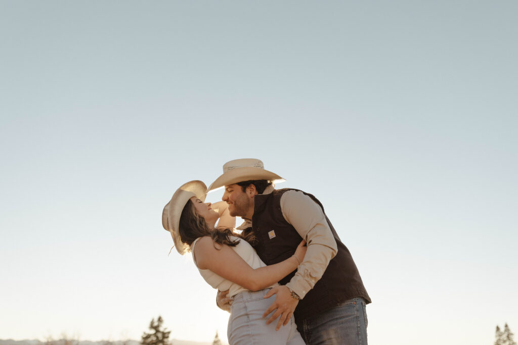 Engagement couple hugging each other and laughing while wearing cowboy hats in Truckee