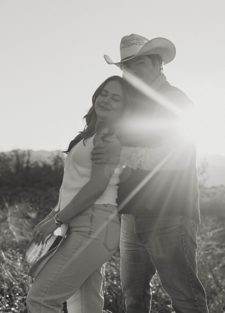 Man holding fiancé while she leans on him with her eyes close and sun glare in background in Truckee