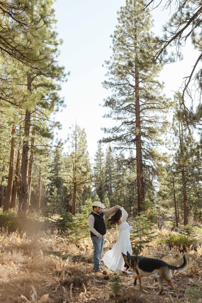 Man twirling fiancé while engagement couple stand in dry grass field with pine trees in background in Truckee