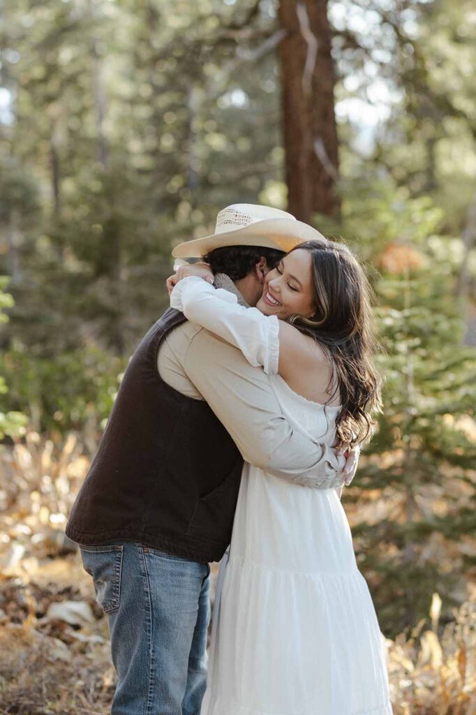 Engagement couple hugging while woman smiles with pine trees in background in Truckee