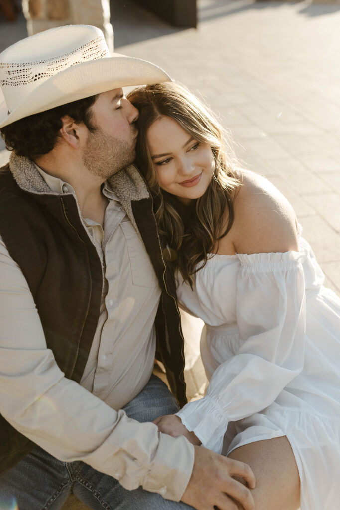 Engagement couple sitting on stone walkway while man kisses fiancé's head in Truckee