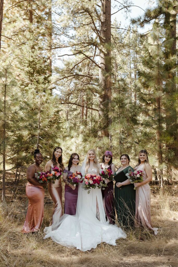Bride and bridesmaids holding colorful floral bouquets while standing between pine trees at Valhalla in Lake Tahoe