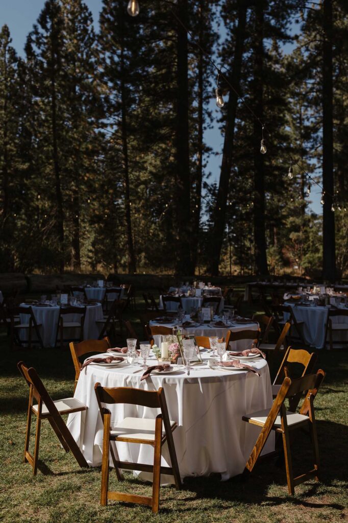 Wedding reception table with wooden chairs on grass with pine trees in background at Valhalla in Lake Tahoe