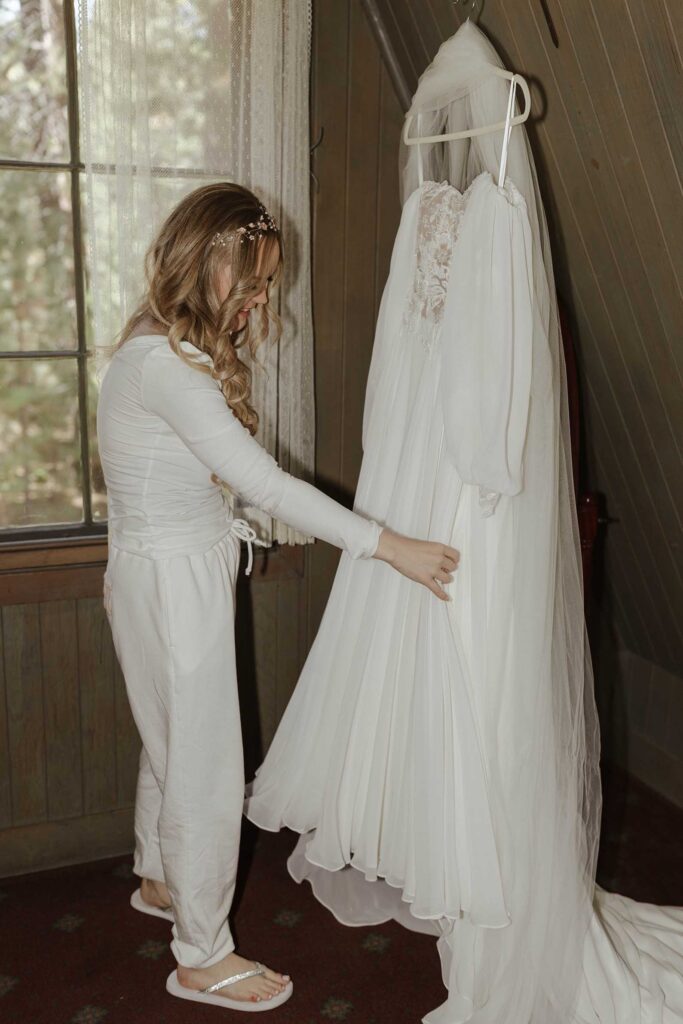 Bride looking at wedding dress hanging on hangar in front of wooden paneling at Valhalla in Lake Tahoe