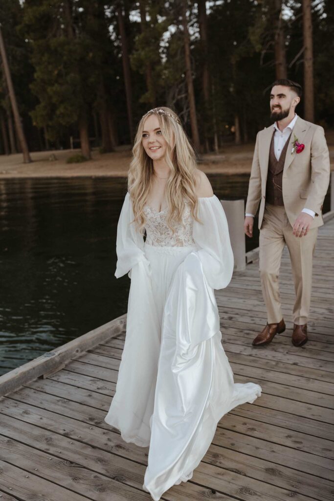 Wedding couple walking along wooden dock at Lake Tahoe while smiling 