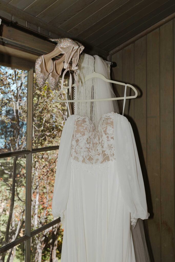 Wedding dress hanging on white hangar next to bride's shoes in front of wooden paneling at Valhalla in Lake Tahoe