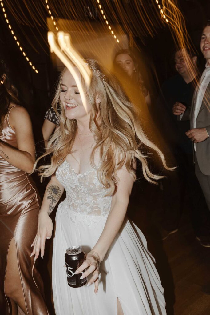 Bride holding drink while dancing during wedding reception with string lights at Valhalla in Lake Tahoe