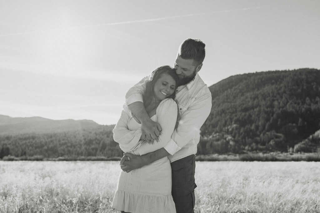 Couple holding hands while arms are wrapped around each other and smiling in golden grass field in Lake Tahoe