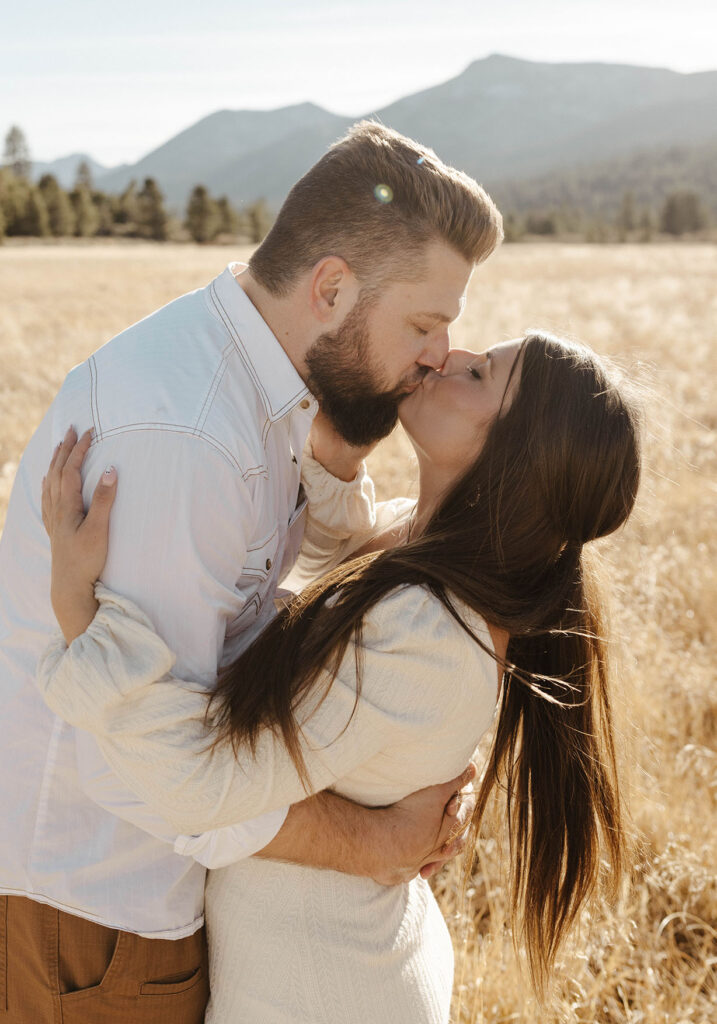 Couple kissing and holding each other while in golden grass field in Lake Tahoe with mountains and trees in background