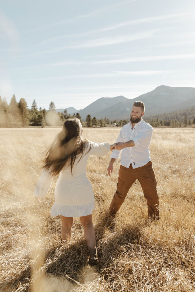 Couple holding hands while swinging around each other in golden field while man smiles at woman in Lake Tahoe