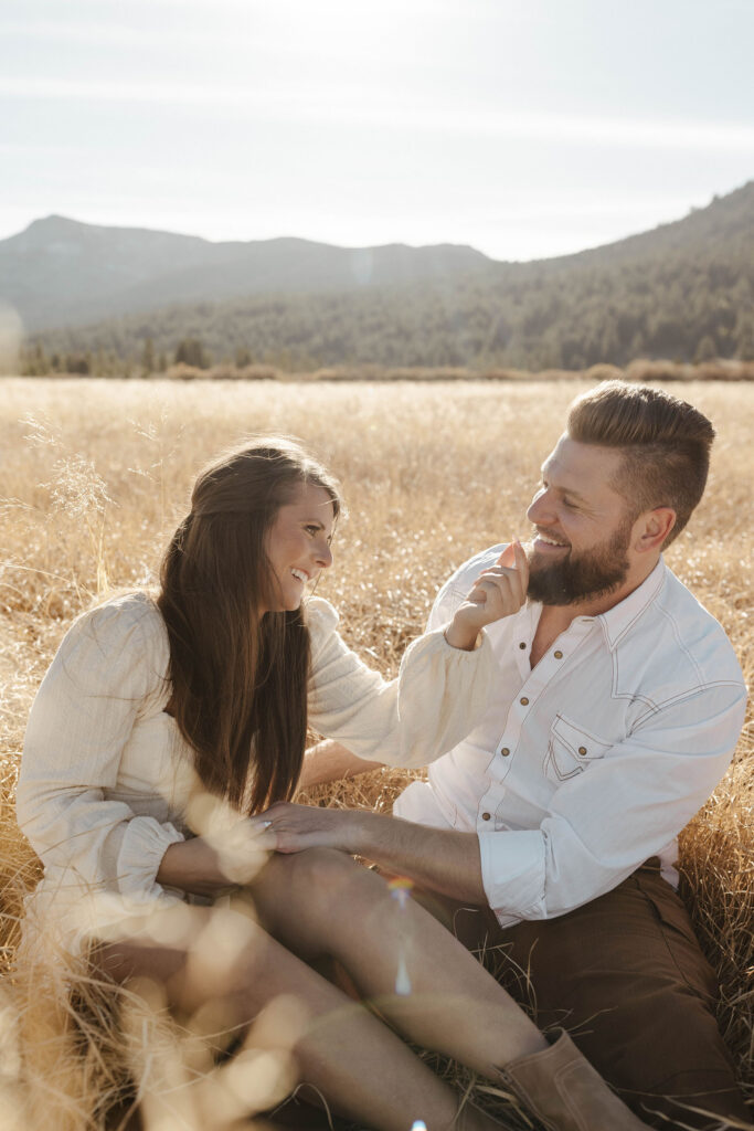 Couple sitting together in golden grass field while smiling and playing with each other in Lake Tahoe