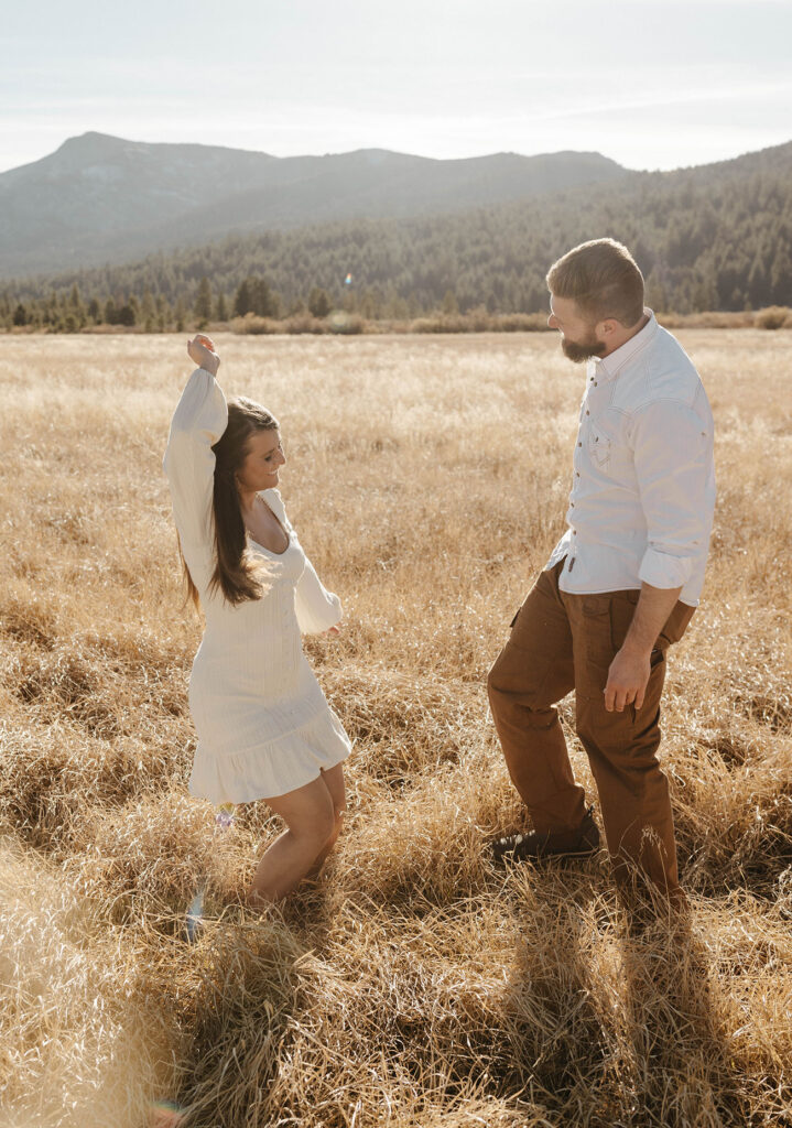 Couple dancing together in golden grass field in Lake Tahoe with trees and mountains in background