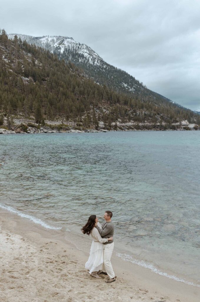 couple dancing on the beach with the water and mountains of lake tahoe behind them 