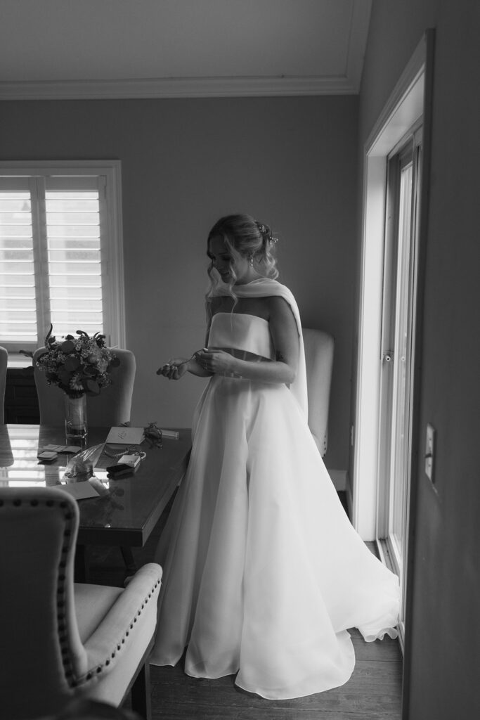 Wedding bride putting on jewelry while standing inside next to table