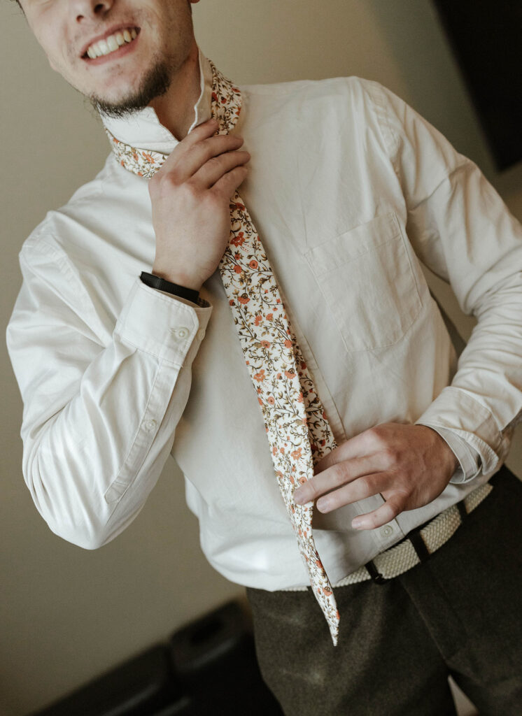 Wedding groom putting on tie before elopement in Emerald Bay