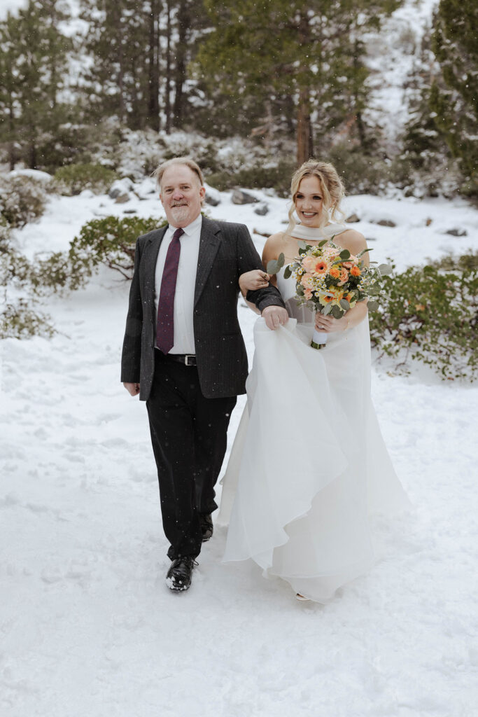 Bride holding dad's arm while smiling and walking down to elopement ceremony in Emerald Bay