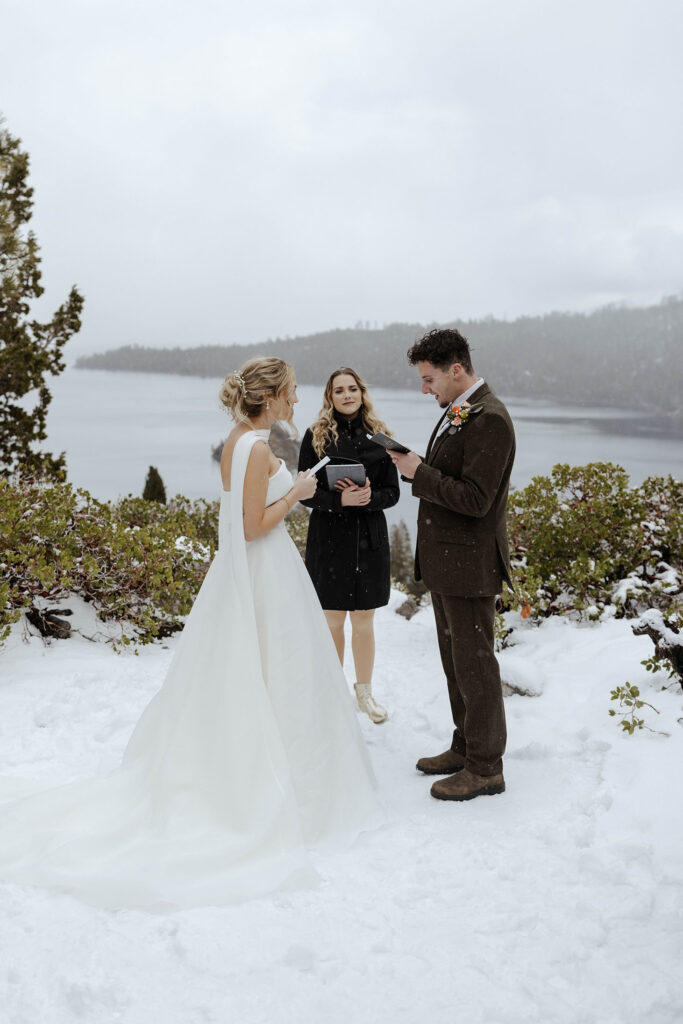 Elopement couple reading vows during ceremony while standing in snow in Emerald Bay with Lake Tahoe in background