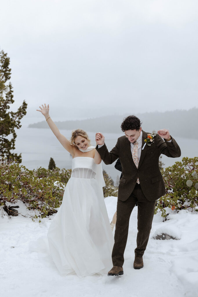Elopement couple holding hands and celebrating while standing in snow after ceremony in Emerald Bay