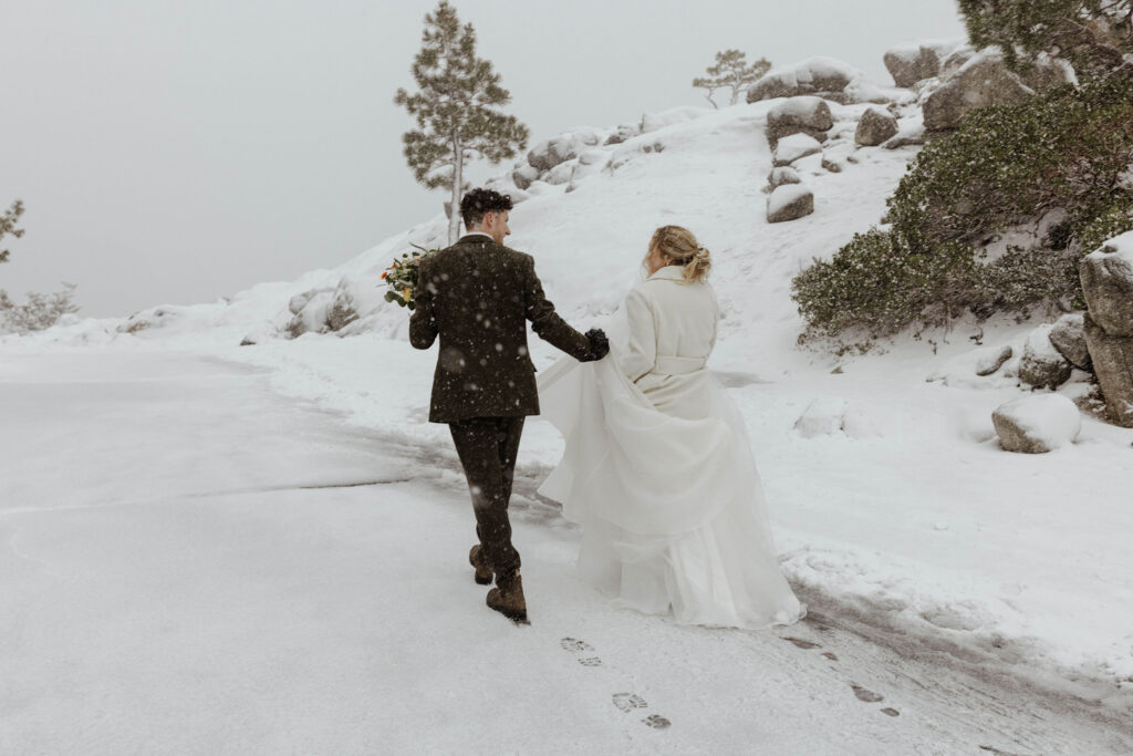 Elopement couple holding hands while walking up snowy hill together away from camera in Emerald Bay