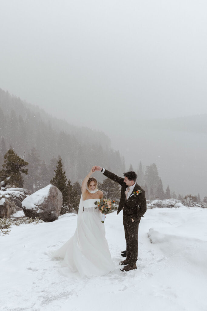 Groom twirling bride in snow while holding hands in Emerald Bay with Lake Tahoe and trees in background