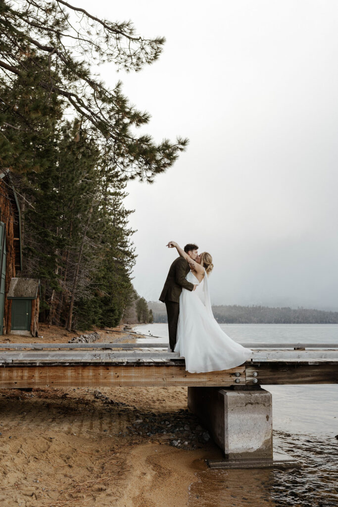 Elopement couple holding each other while kissing on a pier with Lake Tahoe and trees in background