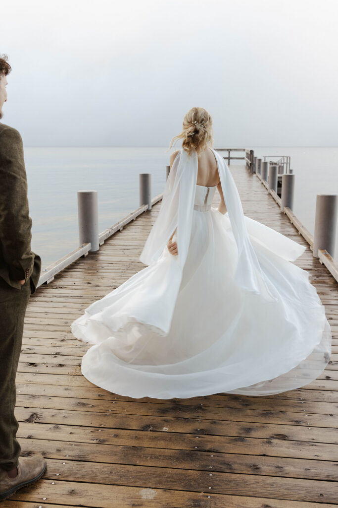 Bride twirling wedding dress while on wooden pier at Emerald Bay with Lake Tahoe in background
