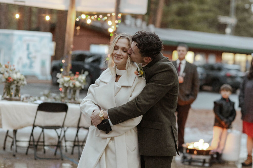 Groom hugging bride from behind and kissing her cheek during elopement reception in Emerald Bay