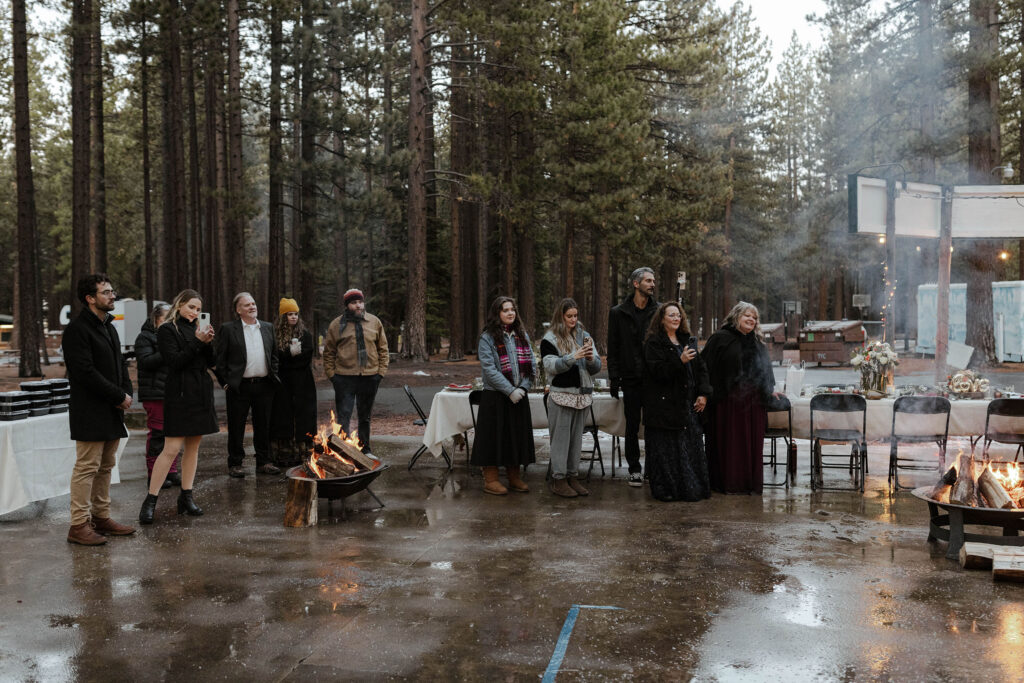 Elopement guests standing around fire and watching couple during reception in Emerald Bay