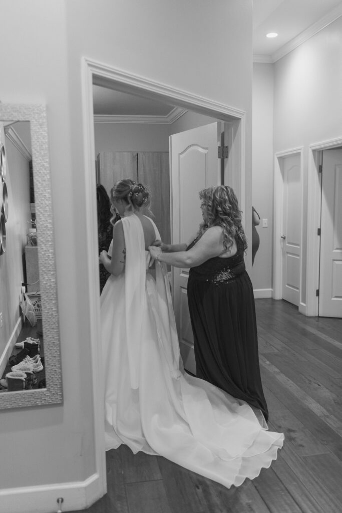 Bride's mom buttoning the back of bride's wedding dress while standing in open doorway