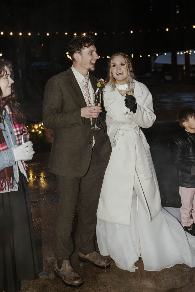 Elopement couple holding drinks while standing around fire pit with guests during reception in Emerald Bay