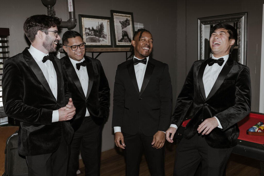 Wedding groom laughing with groomsmen in wedding attire inside at the Tannenbaum