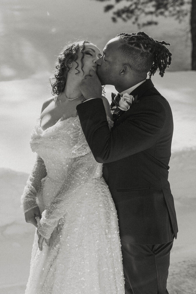Wedding couple kissing while groom hugs bride from behind with snow in background