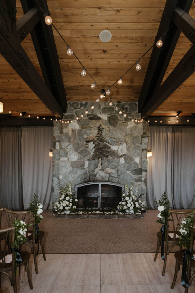 Wedding ceremony overview at the Tannenbaum with stone fireplace and white floral bouquets and string lights above