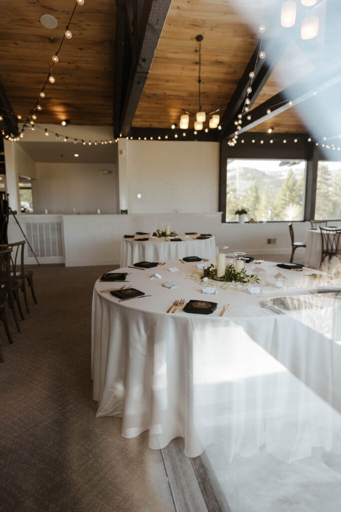 Wedding reception overview at the Tannenbaum with white tables and florals and string lights above in wooden rafters