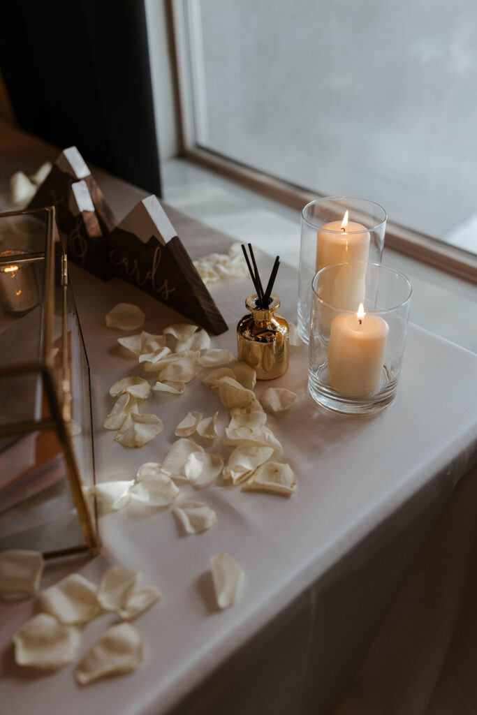 White flower petals scattered across table next to candles in glass and incense
