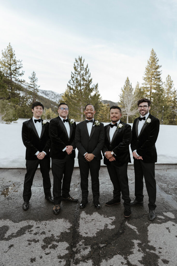 Wedding groom standing and smiling with groomsmen in front of snow bank at the Tannenbaum
