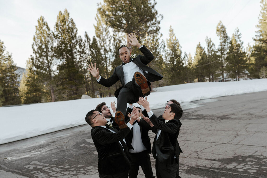 Groomsmen picking up and throwing groom in the air at the Tannenbaum with snow in background