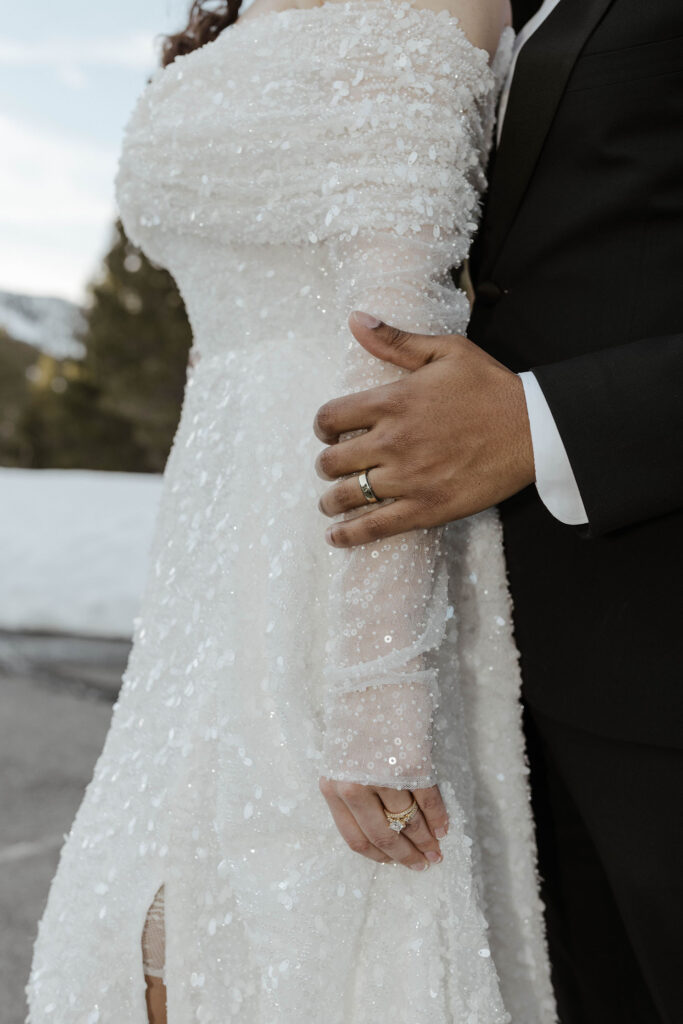 Groom holding bride's arm while both are wearing wedding rings with snow in background