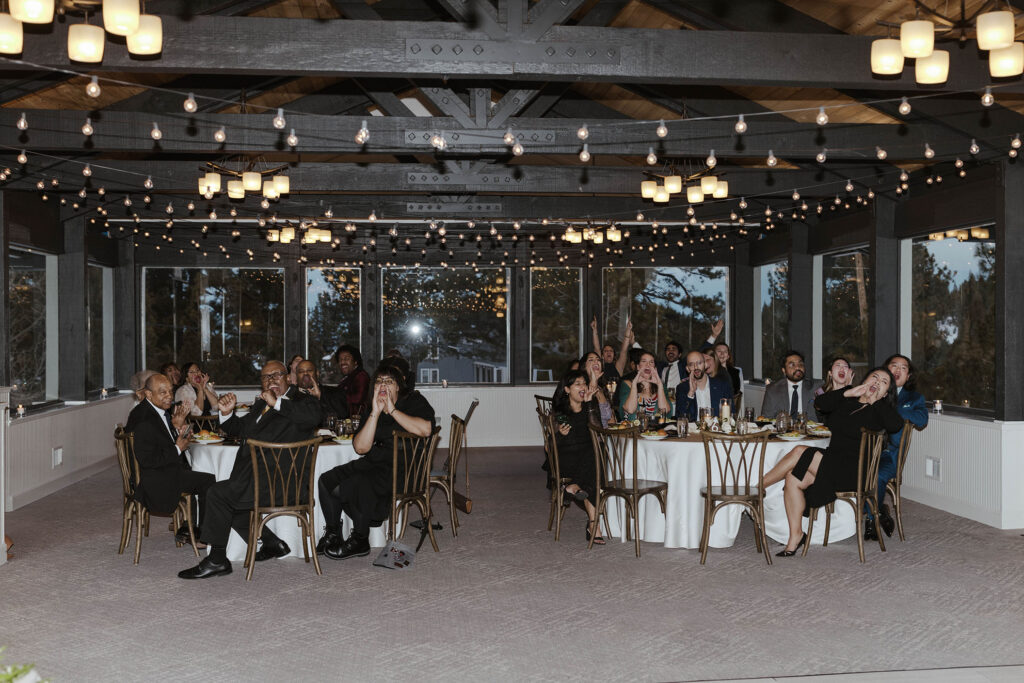 Wedding guests cheering during reception at the Tannenbaum with string lights hanging from rafters and windows in background