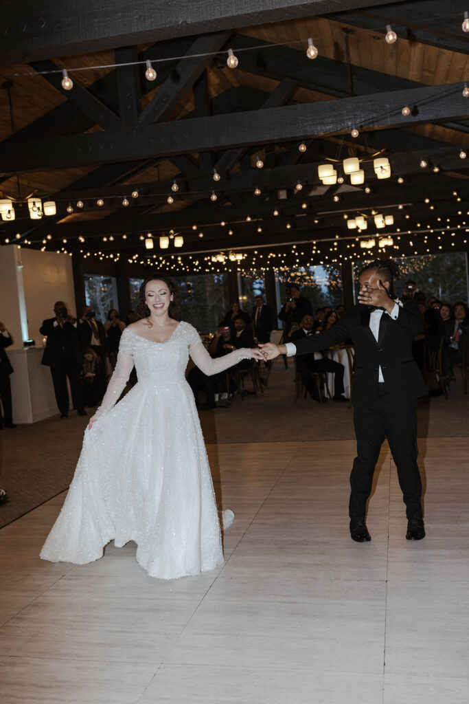 Wedding couple holding hands and dancing as bride smiles and guests watch in background during reception at the Tannenbaum