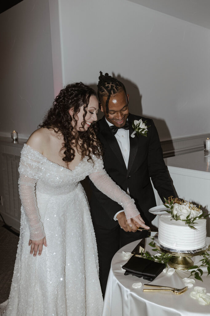 Wedding couple holding knife and cutting cake together with white floral decorations at the Tannenbaum