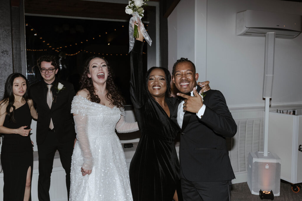 Wedding couple posing with guest who caught floral bouquet and laughing at the Tannenbaum