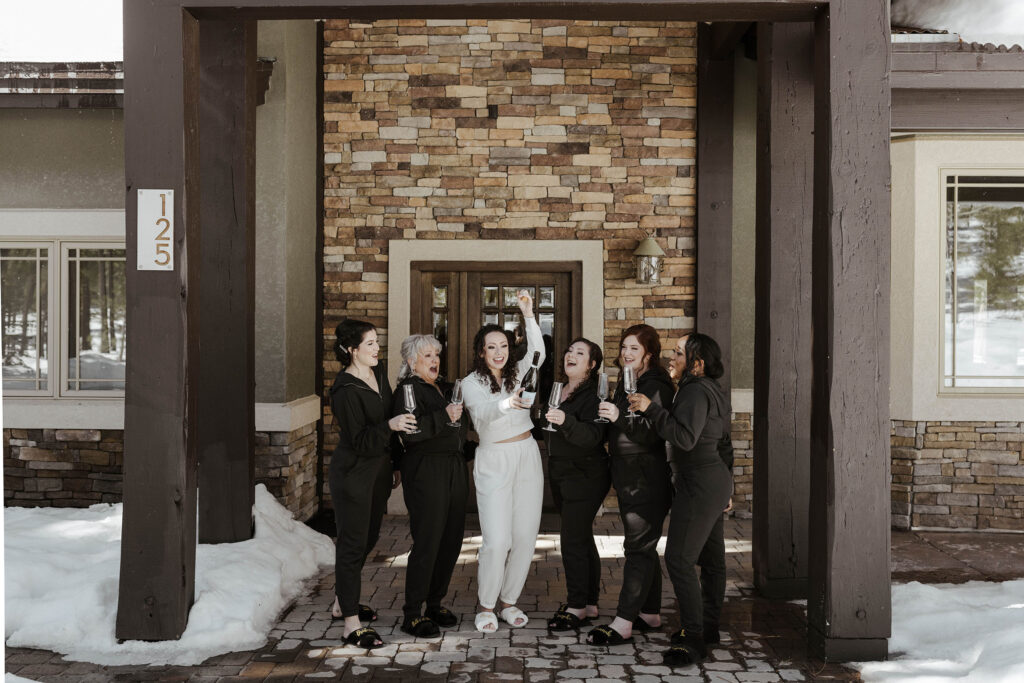 Wedding bride and bridesmaids celebrating with champagne and glasses in front of brick building during winter at the Tannenbaum